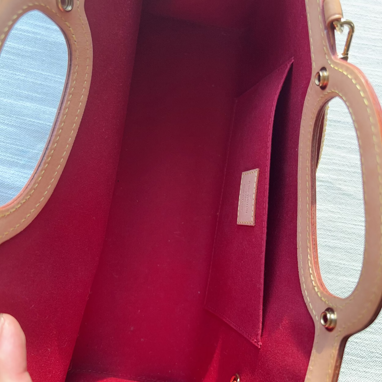 Red handbag with gold handles held by a hand against a light background