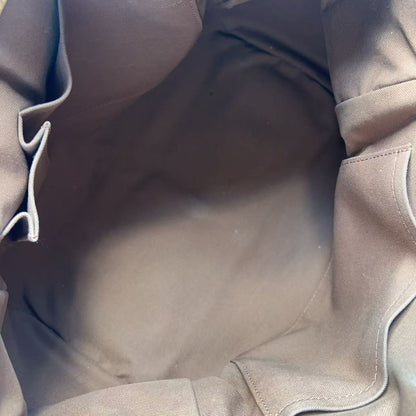 Close-up view of the interior lining of a taupe-brown handbag, showing the fabric texture, stitched compartments, and a small gold metal ring near the bottom.