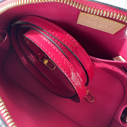 Close-up of a Louis Vuitton handbag interior showing a bright fuchsia pink patent leather lining, matching strap, gold-tone zippers, and a beige leather brand patch on the inside.