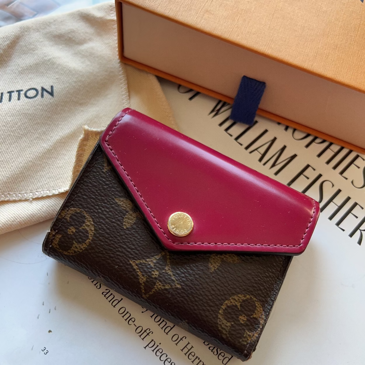 Louis Vuitton wallet with pink flap on a surface with books and packaging.