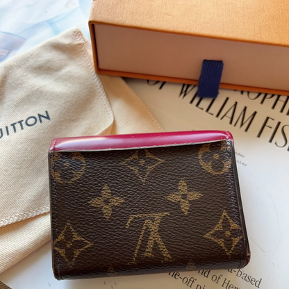 Louis Vuitton wallet with monogram pattern on a surface with a book and fabric.