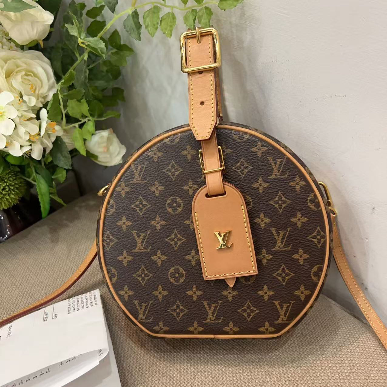 Louis Vuitton monogram handbag on a textured surface with flowers in the background