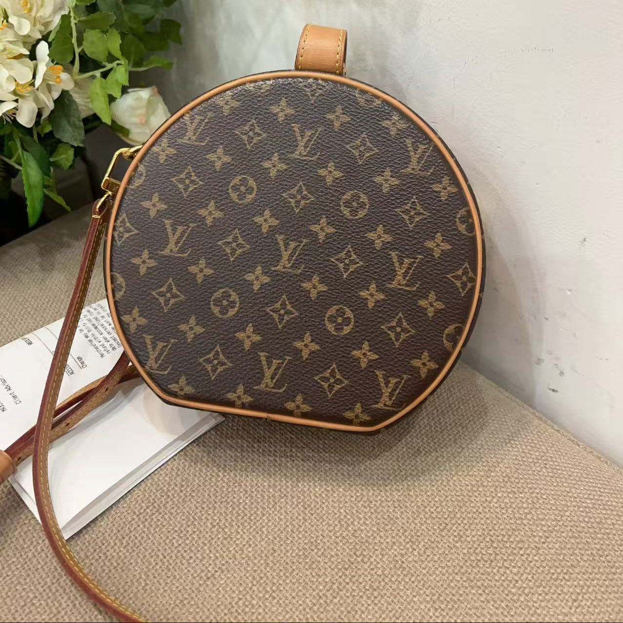 Round handbag with monogram pattern on a surface with flowers in the background