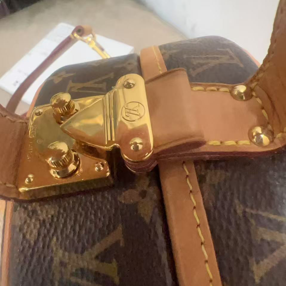 Close-up of a brown leather handbag with gold hardware on a white surface.