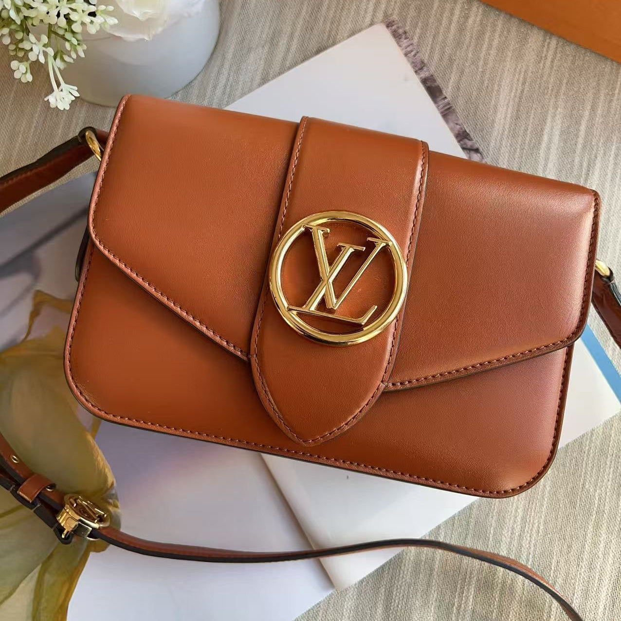 Brown handbag with gold emblem on a surface with flowers and books