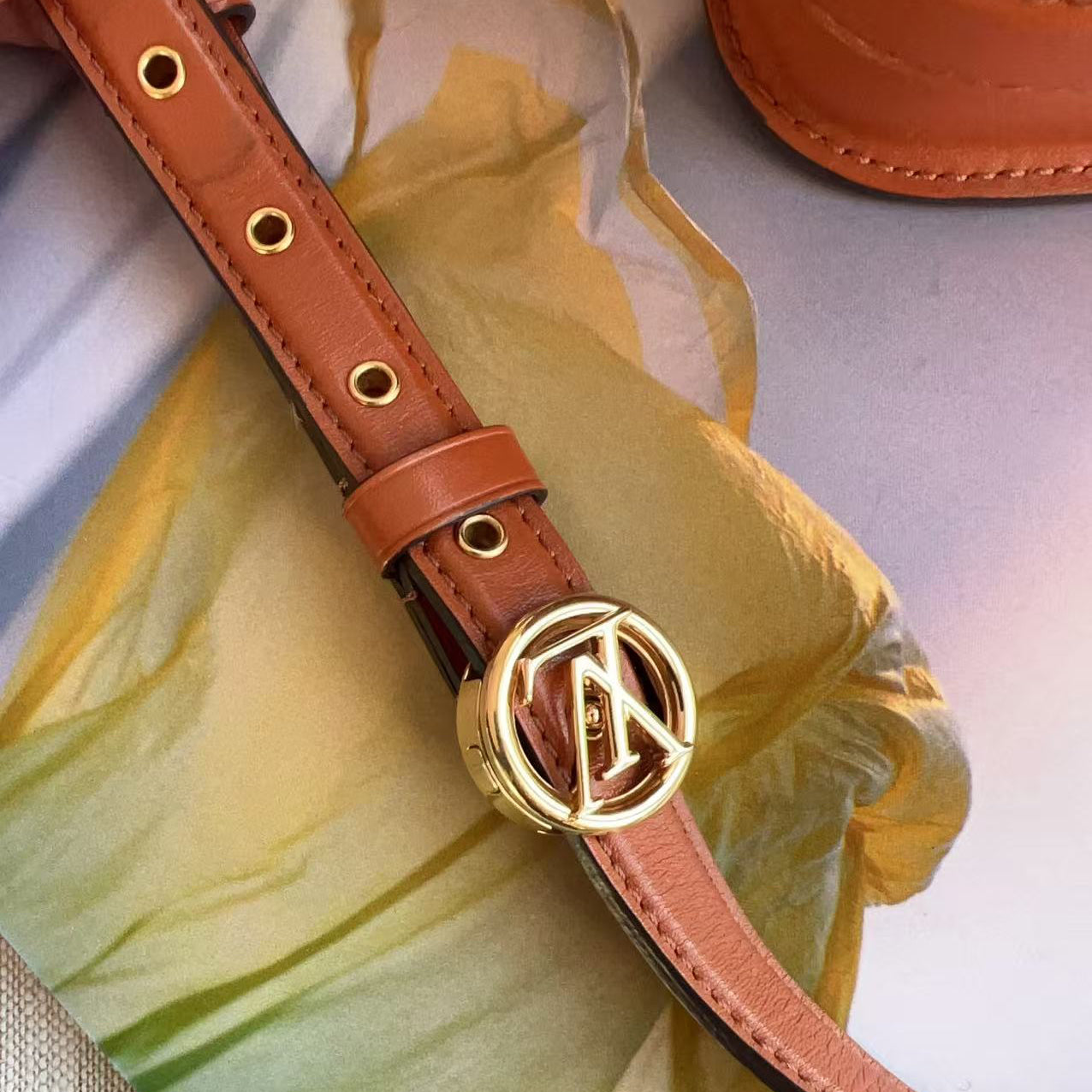 Brown leather belt with gold buckle on a yellow fabric background