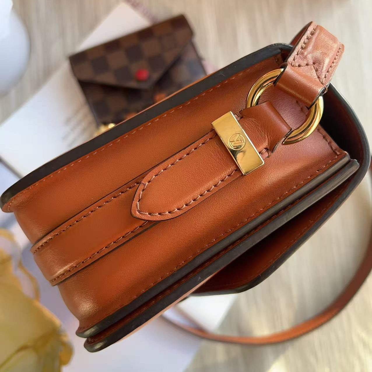 Brown leather handbag with gold clasp on a reflective surface