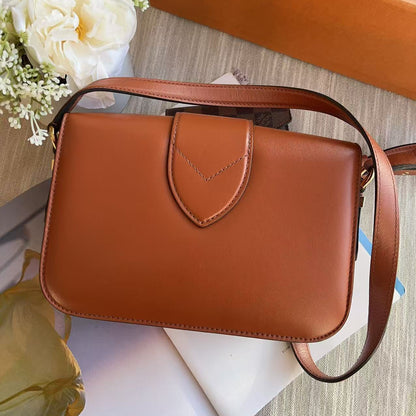 Brown leather handbag on a textured surface with flowers and an orange box in the background