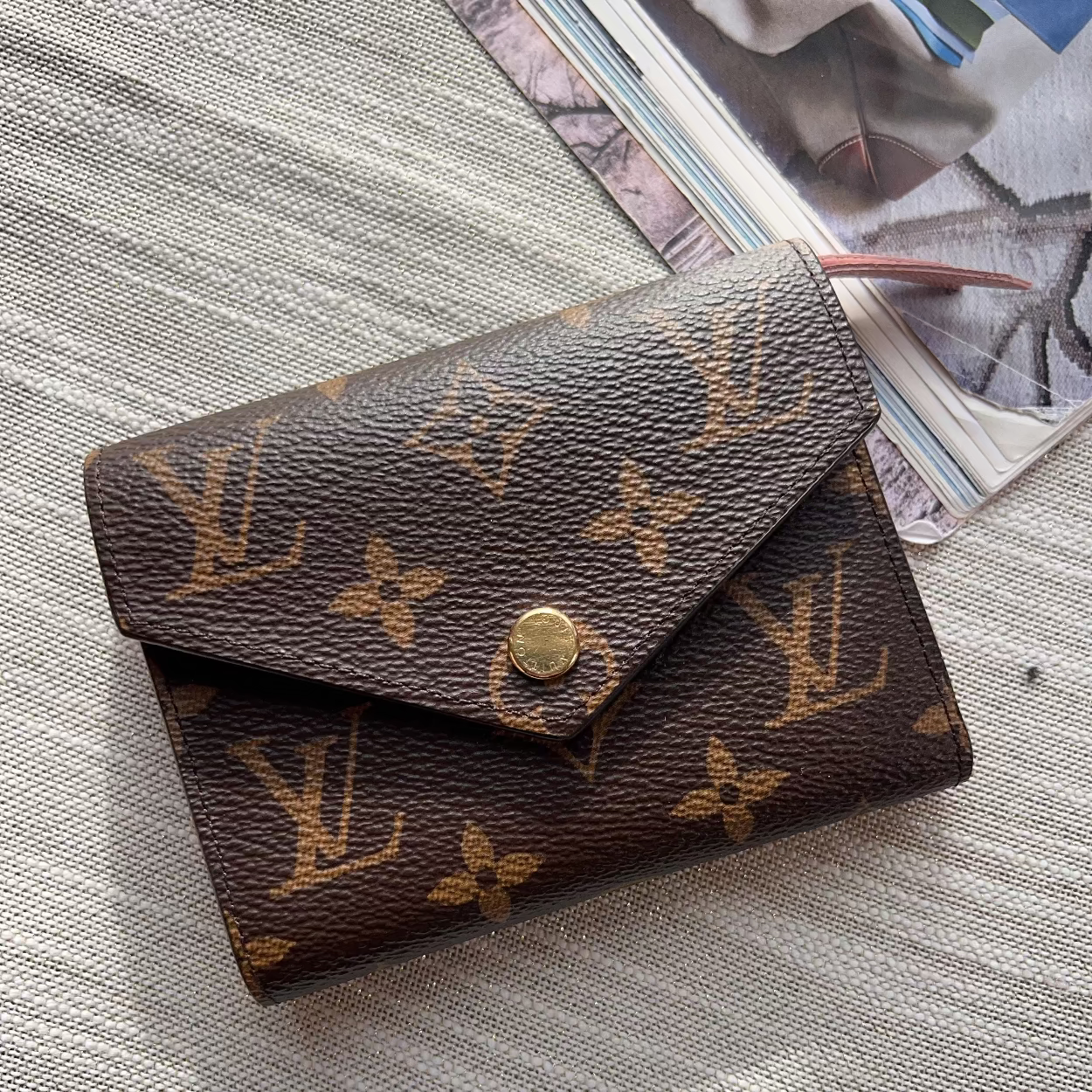 Louis Vuitton wallet on a textured surface with a magazine in the background
