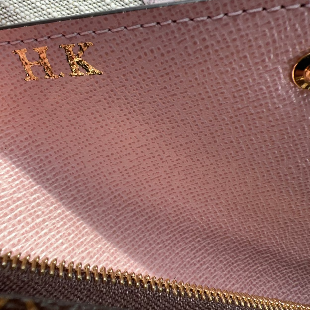 Close-up of a pink wallet with initials 'H.K.' and a gold zipper.