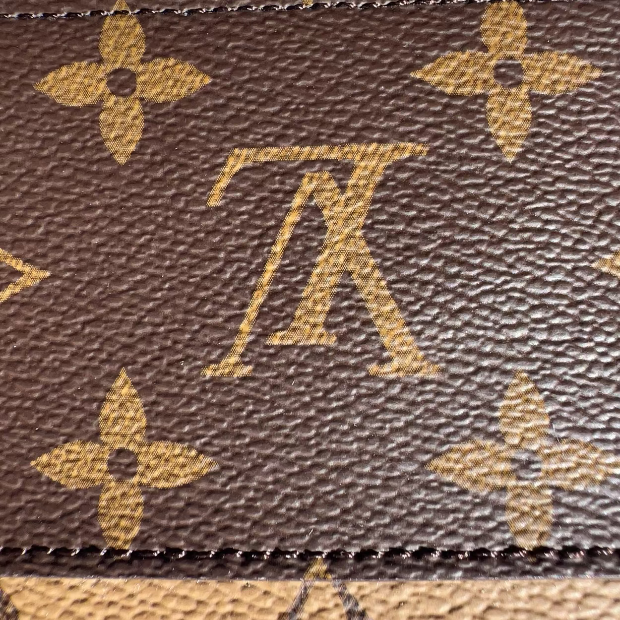 Close-up of a brown leather bag with a prominent logo pattern.