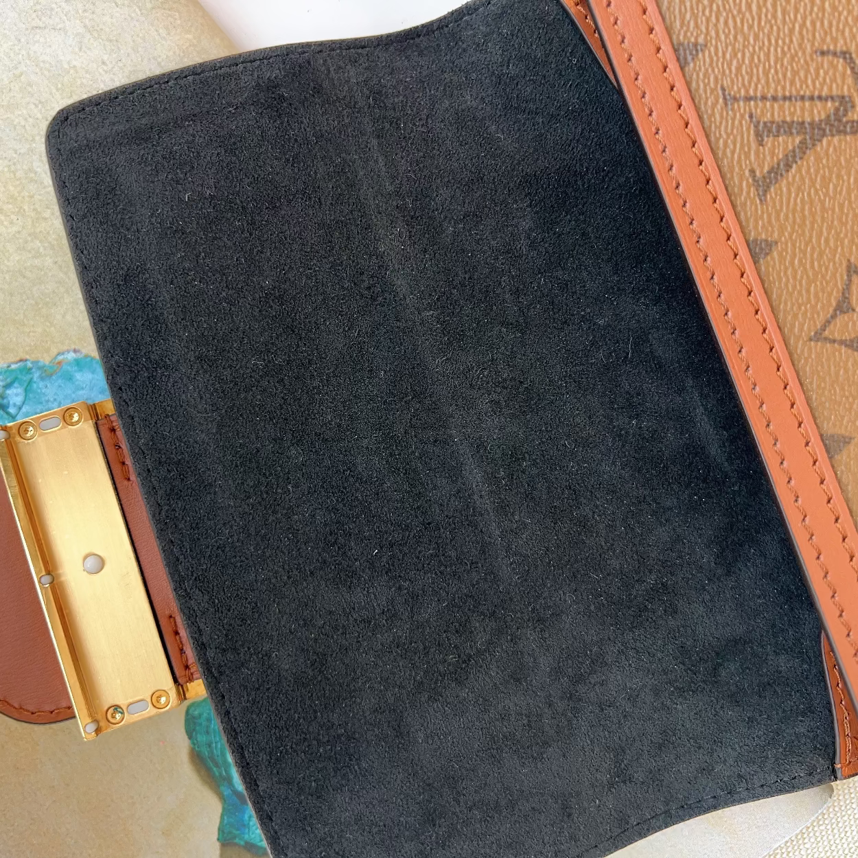 Close-up of a black suede clutch with gold clasp on a patterned surface