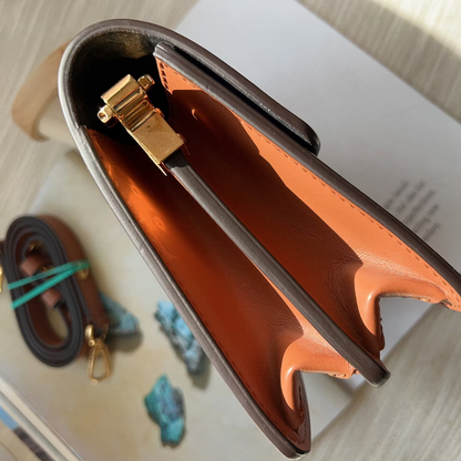 Brown leather pouch with gold clasp on a light wooden surface