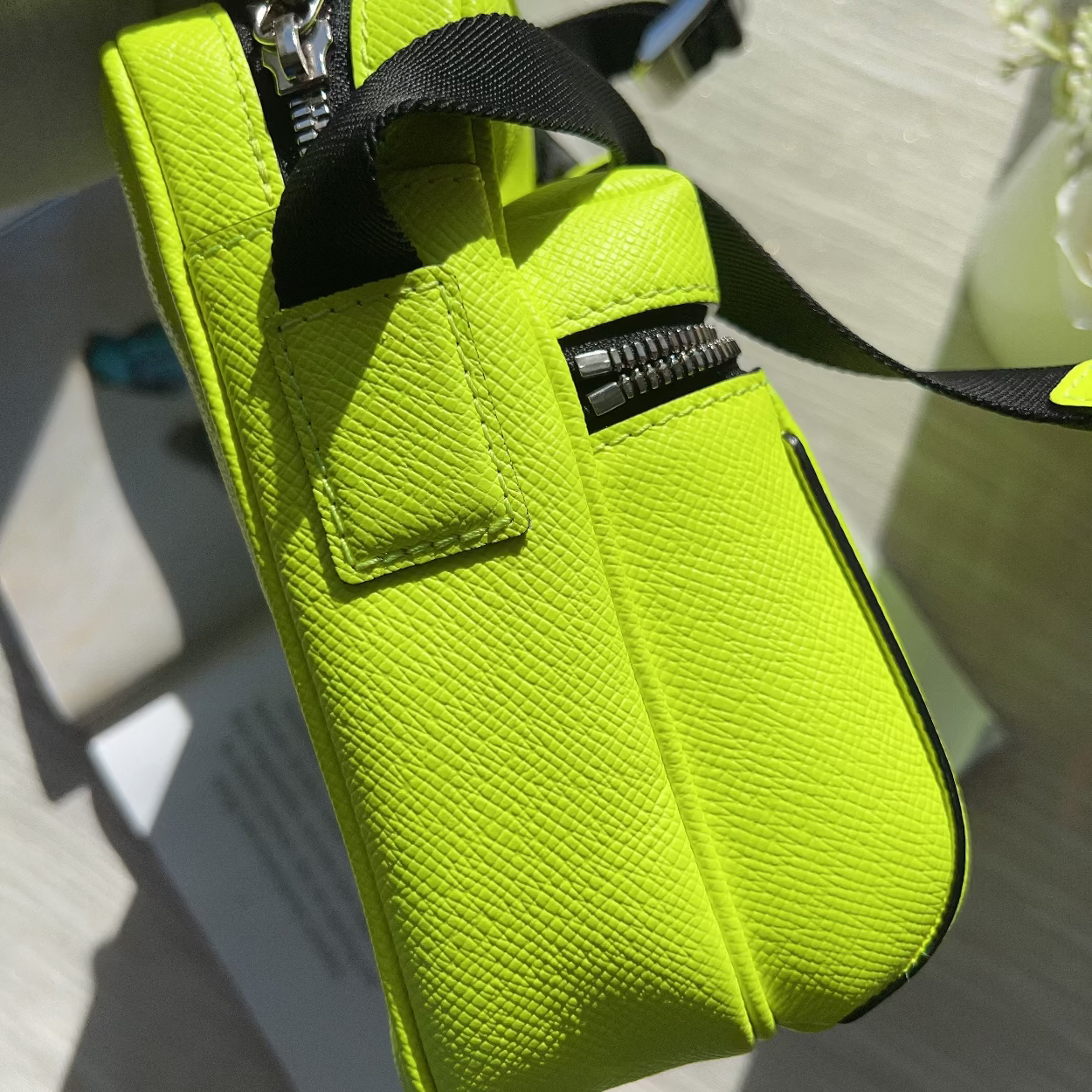 A bright neon yellow-green textured leather pouch bag with black zippers and a black strap, shown in a close-up angled shot.
