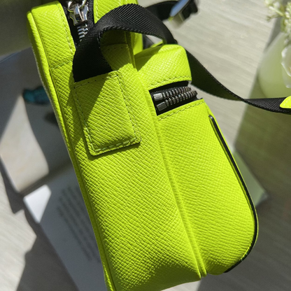 A bright neon yellow-green textured leather pouch bag with black zippers and a black strap, shown in a close-up angled shot.