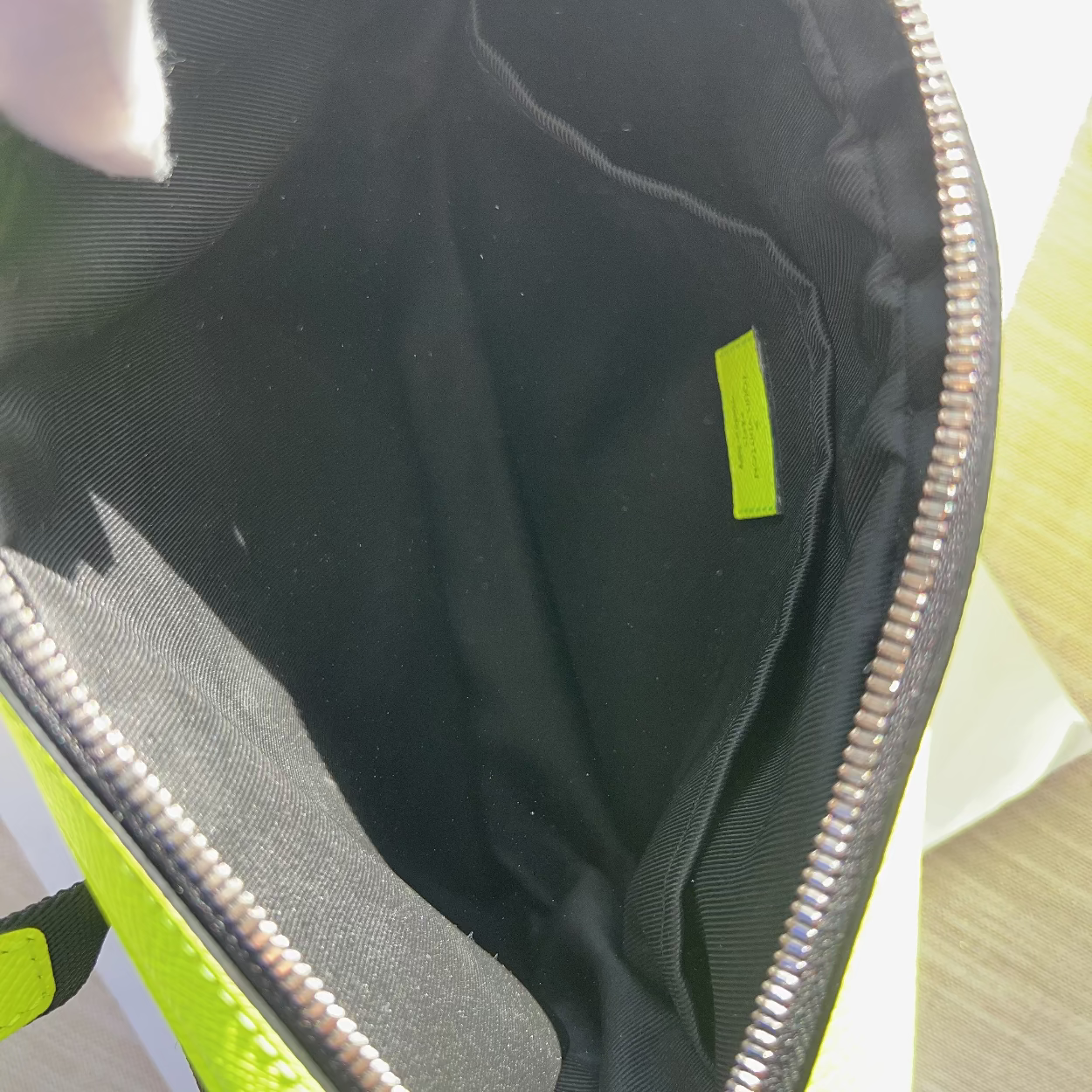 Close-up of the open interior of a bright neon yellow-green bag with a black lining and a small matching neon label inside.