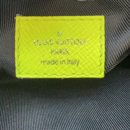 Close-up of a Louis Vuitton Paris made in Italy interior label sewn onto dark gray fabric, with a white gloved finger visible at the top.