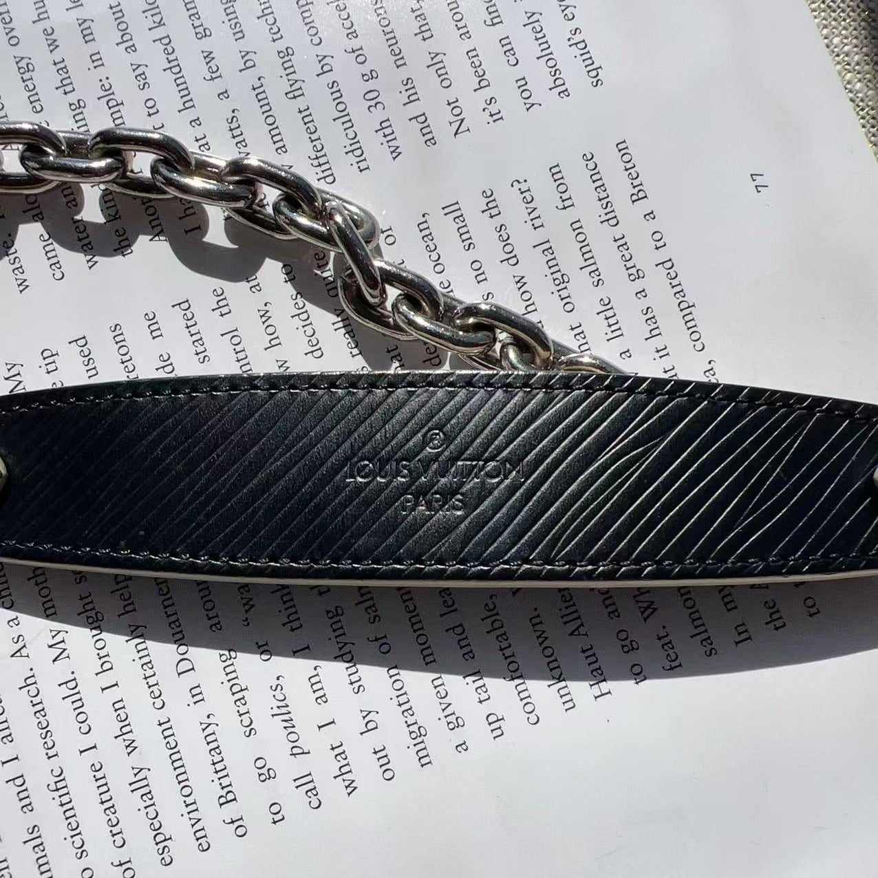 Black textured belt with silver chain on a piece of paper