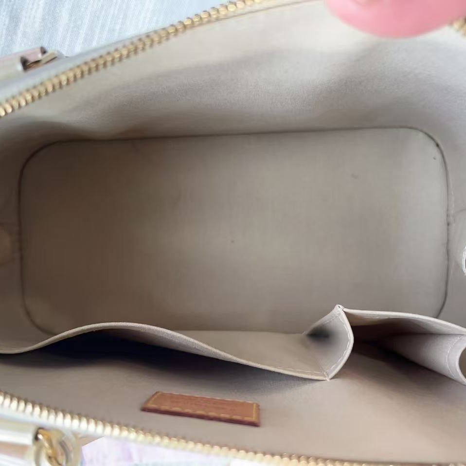 Beige handbag with gold zipper and interior lining, held open by a hand.