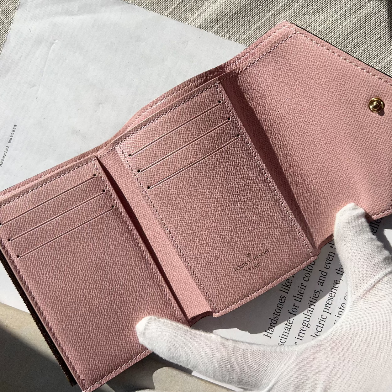 Pink wallet held by a gloved hand on a textured surface