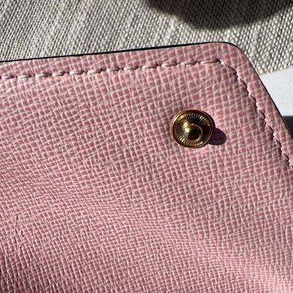 Close-up of a pink textured wallet with a gold button on a textured surface.