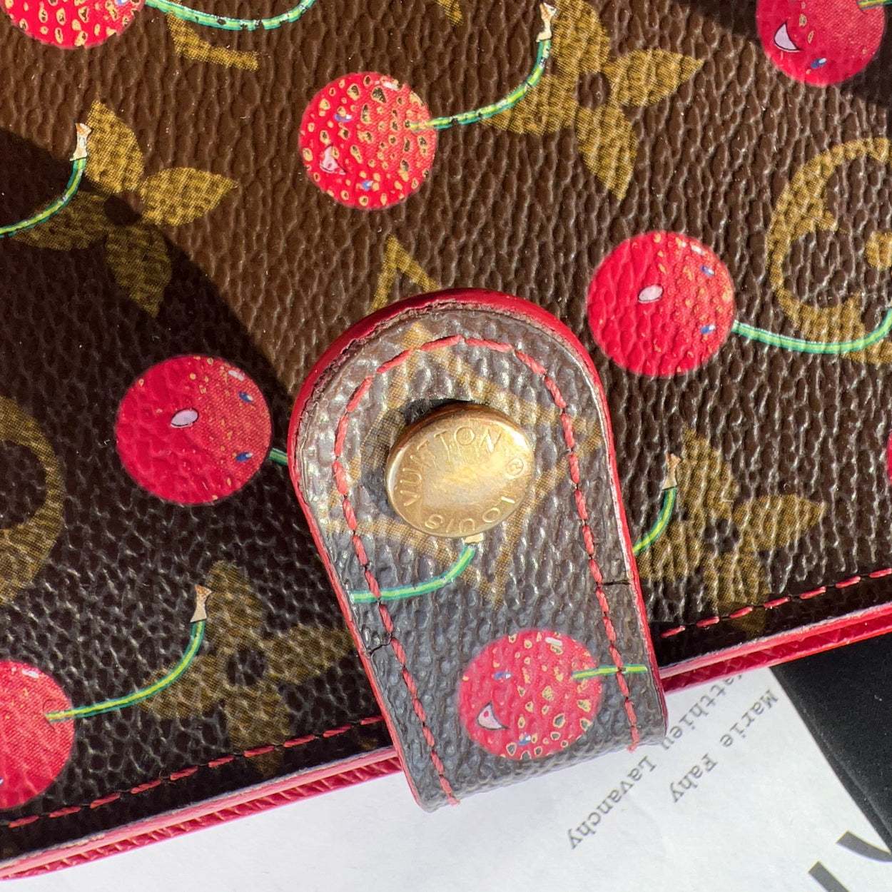 Close-up of a brown leather wallet with red cherry pattern and gold buckle.