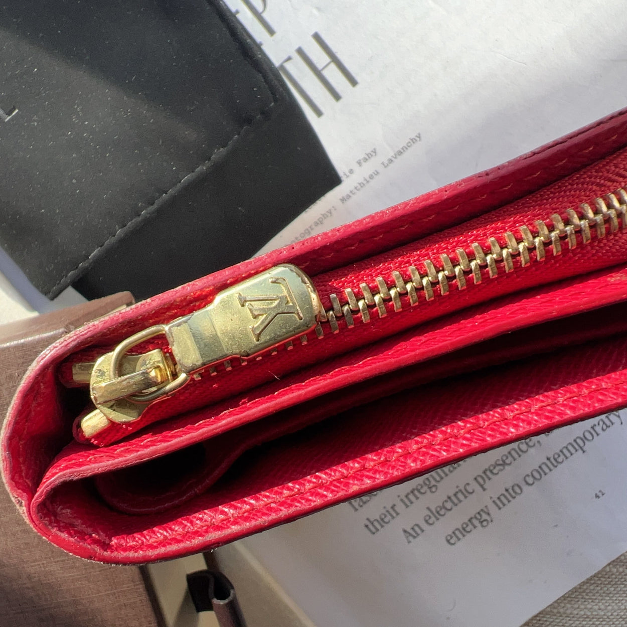 Red wallet with gold zipper on a surface with a Chanel box in the background