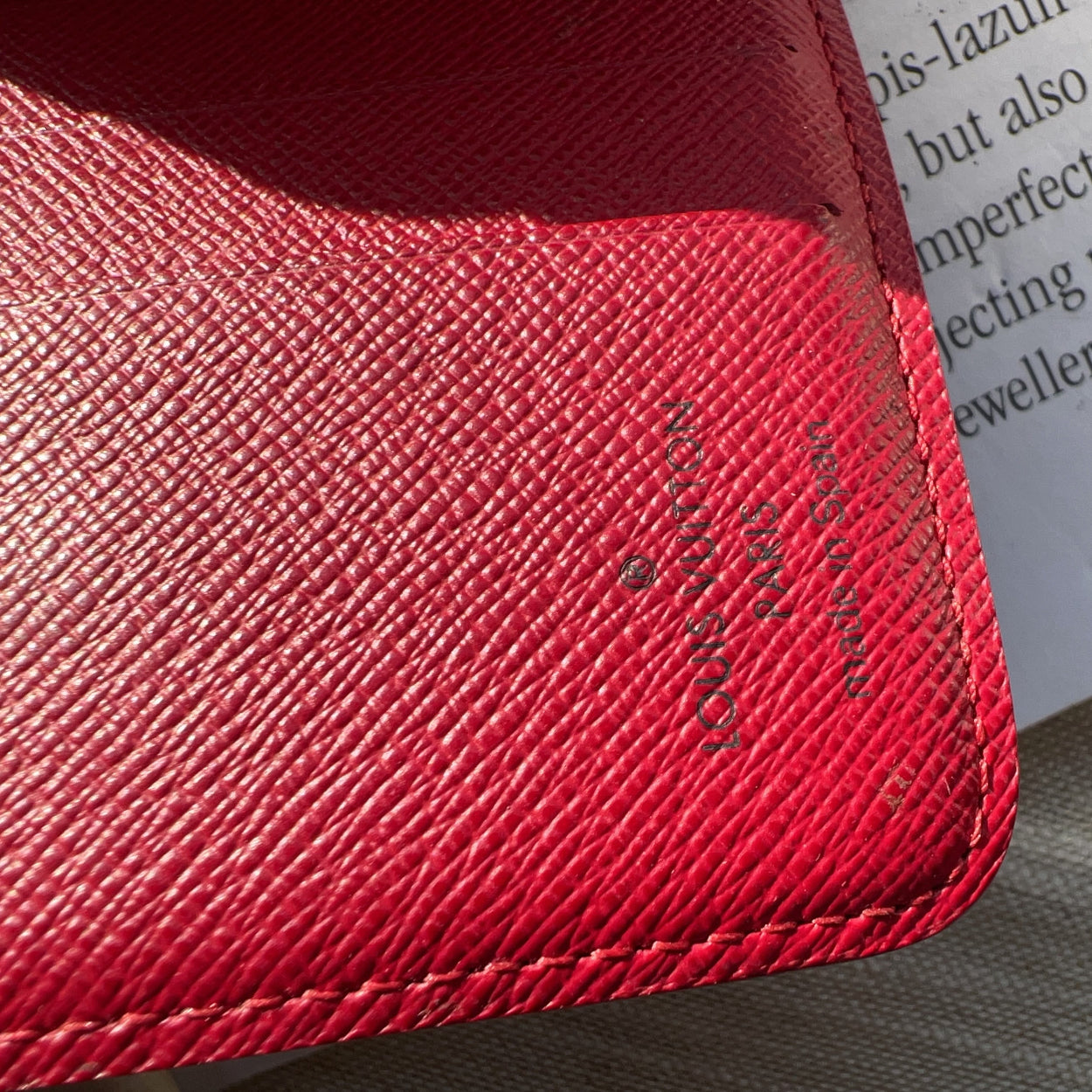 Close-up of a red textured wallet with a brand logo, placed on a surface with text.
