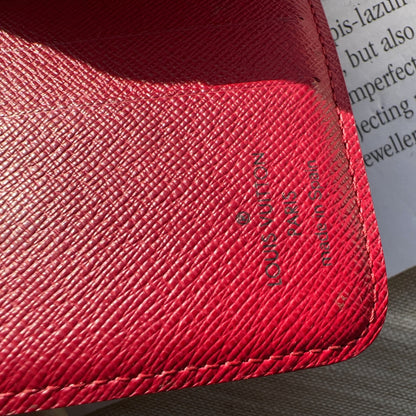 Close-up of a red textured wallet with a brand logo, placed on a surface with text.