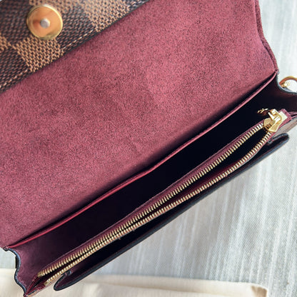 Close-up of a maroon clutch bag with gold zipper and patterned fabric on top.