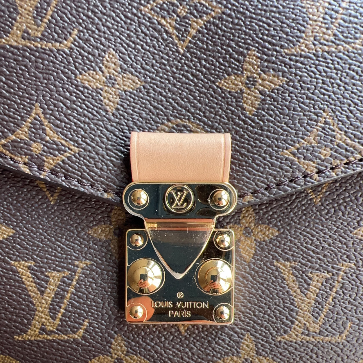 Close-up of a Louis Vuitton bag with a gold clasp on a monogrammed background