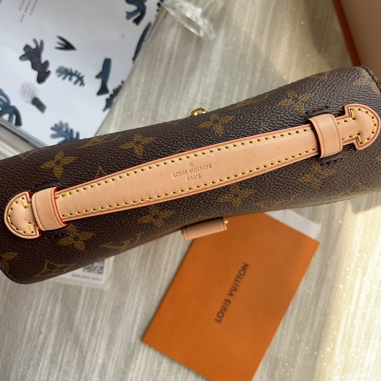 Louis Vuitton handbag with monogram pattern and tan leather handle on a glass surface.