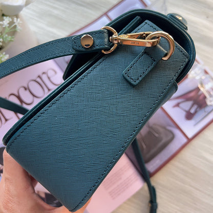 Green handbag with gold hardware held by a hand on a blurred background