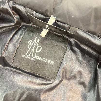 Close-up of a black Moncler Grenoble puffer jacket interior, showing the black brand patch with white logo text and a white size tag sewn onto the collar.