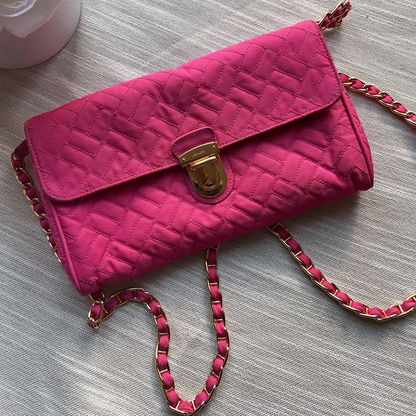 Pink quilted handbag with a gold clasp on a light gray surface