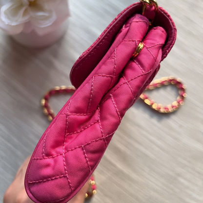 Pink quilted handbag held by a hand on a light surface with flowers in the background