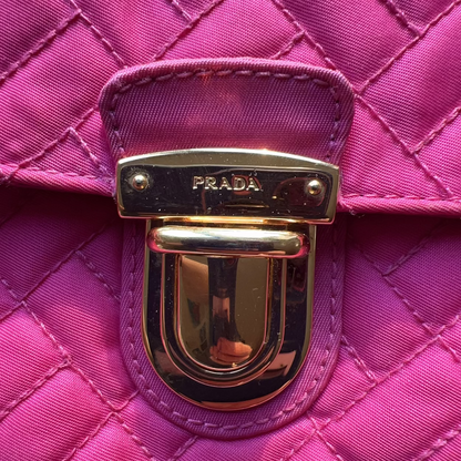 Close-up of a pink quilted handbag with a gold Prada clasp.