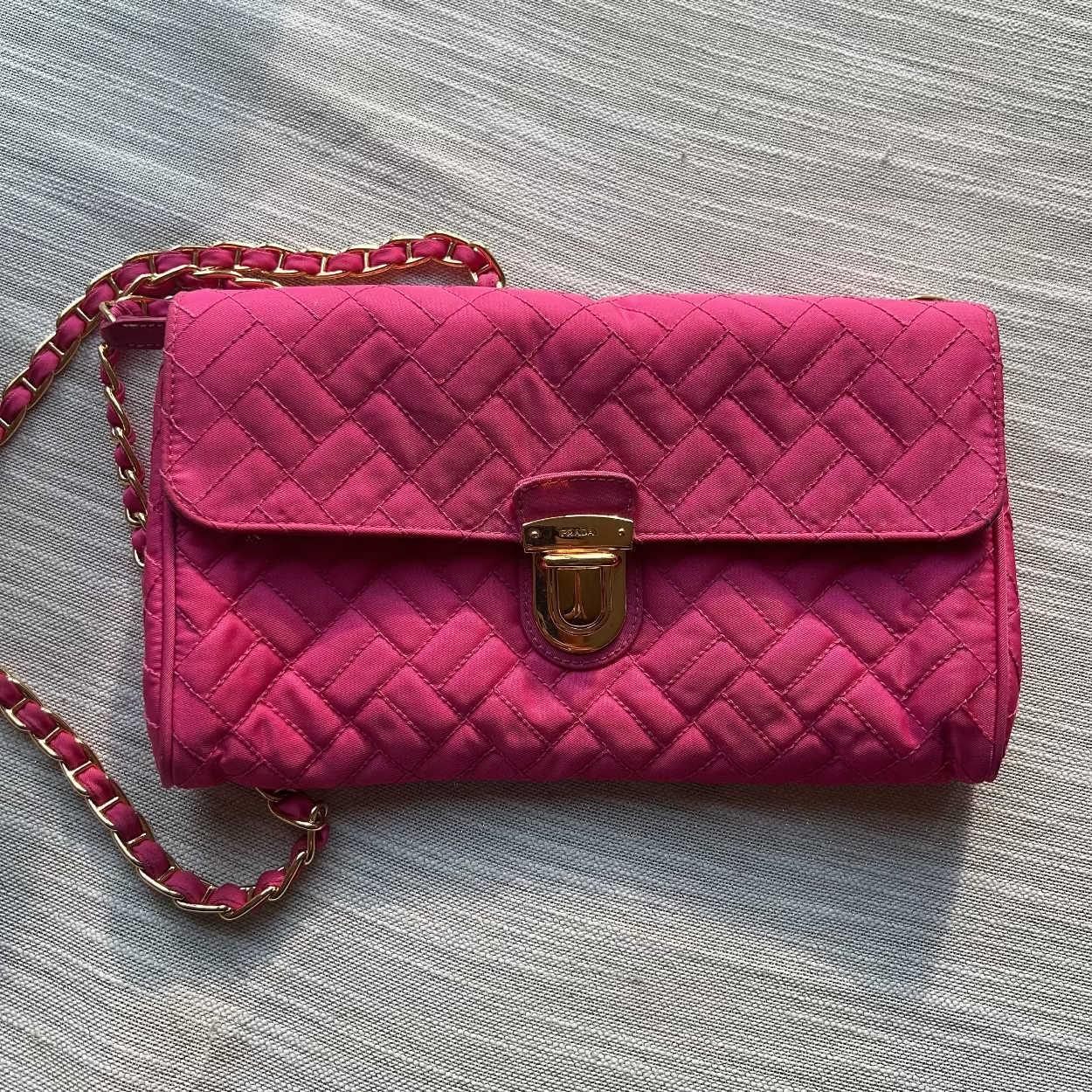 Pink quilted handbag with a gold clasp on a gray surface