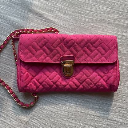 Pink quilted handbag with a gold clasp on a gray surface