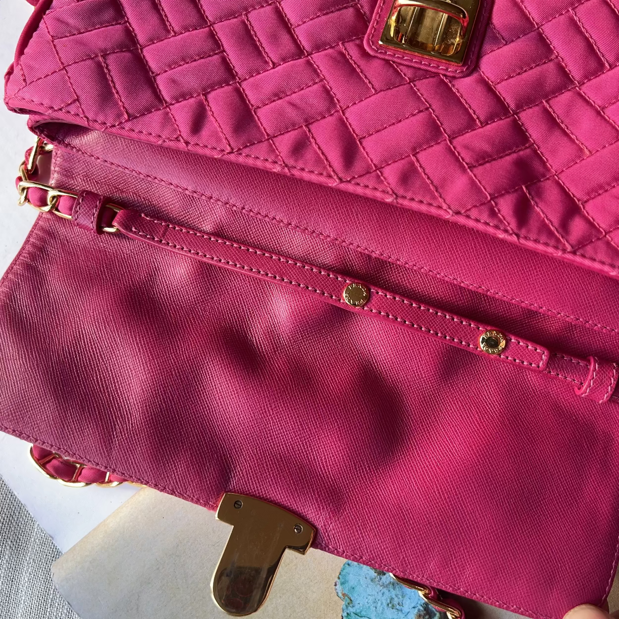 Close-up of a pink handbag with gold accents on a textured surface
