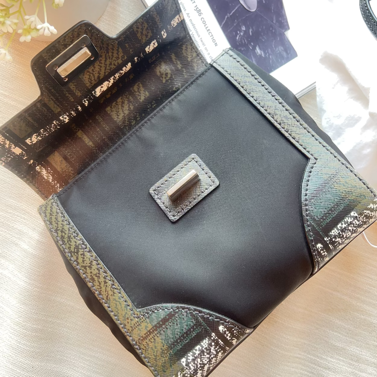 Black leather clutch bag with gold accents on a light wooden surface.