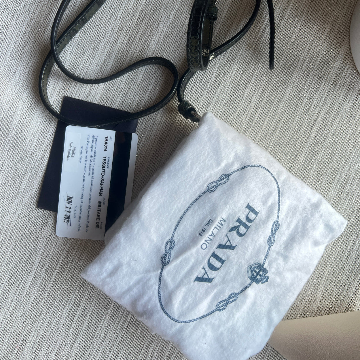 Black leather strap with Prada branded pouch on a textured surface
