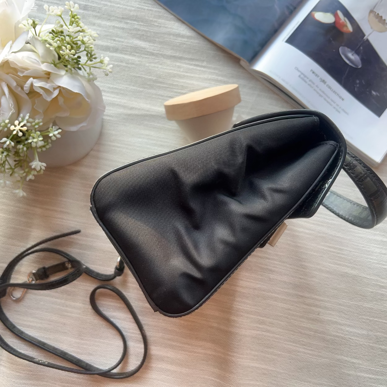 Black sleep mask on a light wooden surface with flowers and a book in the background