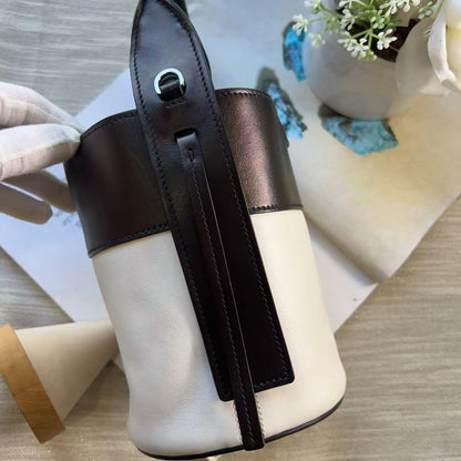 A color-blocked leather handbag with a white and dark brown body, featuring a dark brown leather strap across the front and a small white flower in a vase in the background.