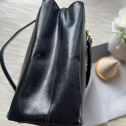 A black textured leather handbag shown from a top-down angle on a light wood surface, with a white sheet of paper and small decorative props underneath.