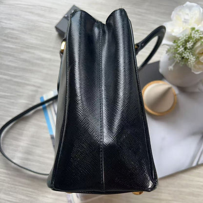 A black textured leather handbag shown from a top-down angle on a light wood surface, with a small vase of flowers and papers in the background.