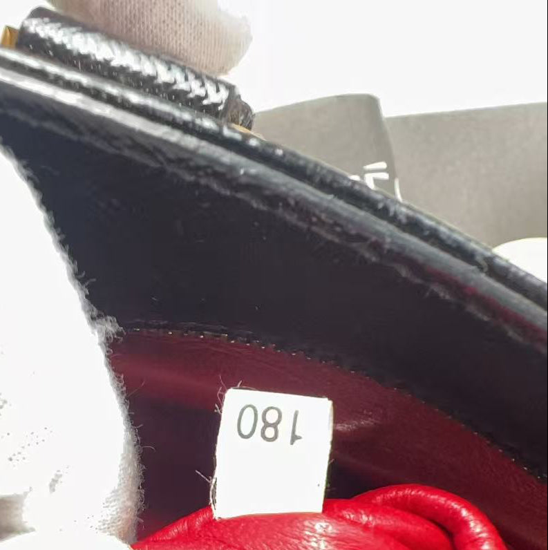 Close-up of the interior of a black leather handbag with a bright red lining, showing a white price tag marked '180' and a white gloved hand holding the opening.