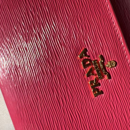 A close-up of a bright pink textured leather notebook cover with gold-tone 'A DAY K' lettering, resting on a white book page.