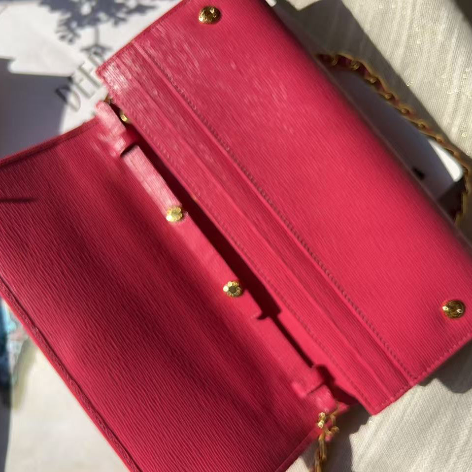 A bright pink textured leather clutch bag with gold-tone hardware and a gold chain strap, shown open on a light-colored textured fabric surface.