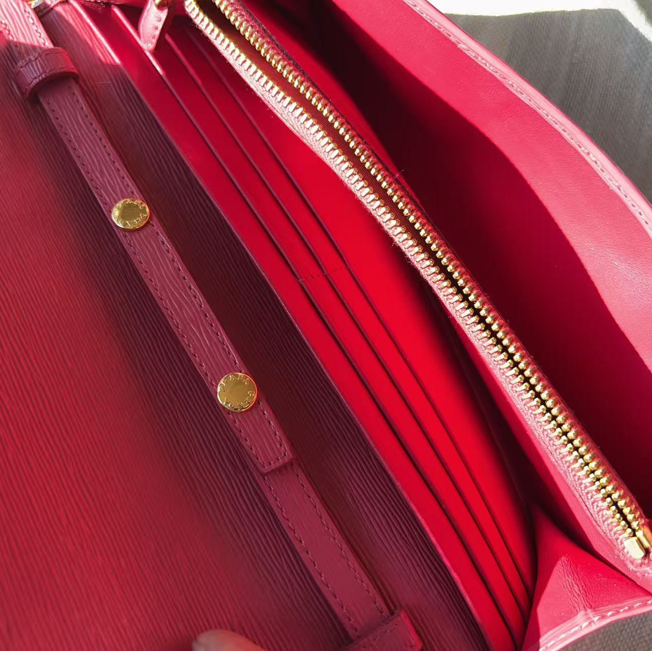Close-up of a red leather handbag showing the interior, including a gold zipper, card slots, and a matching red strap with gold-tone rivets.